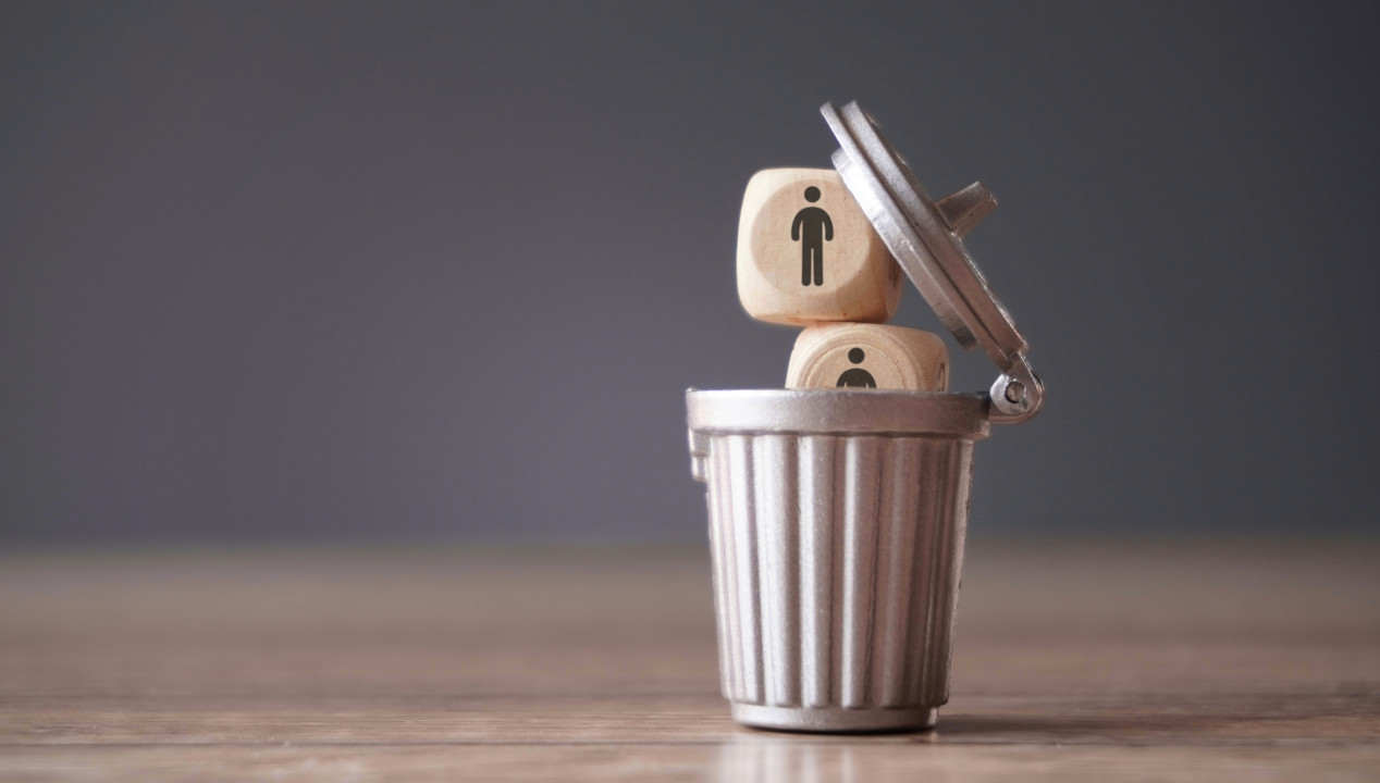 Mülleimer, in den zwei Würfel mit symbolischen Männerfiguren fallen