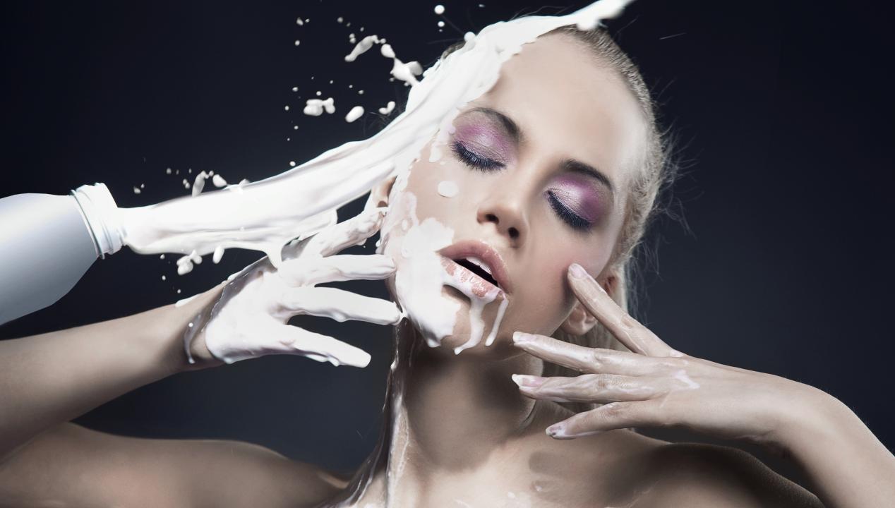 Frau mit geschlossenen Augen lässt sich für einen Fake Cumshot beim Camsex mit Milch im Gesicht bespritzen