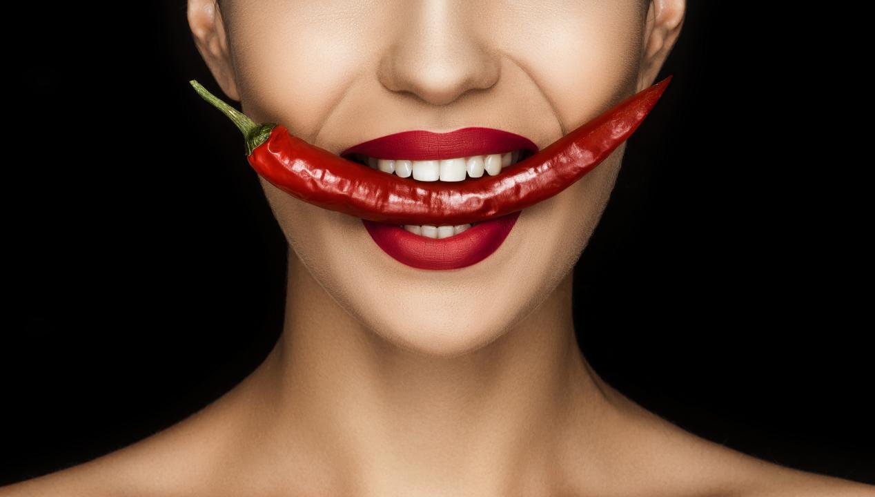 attraktive Frau mit roten Lippen beißt auf eine rote Chili