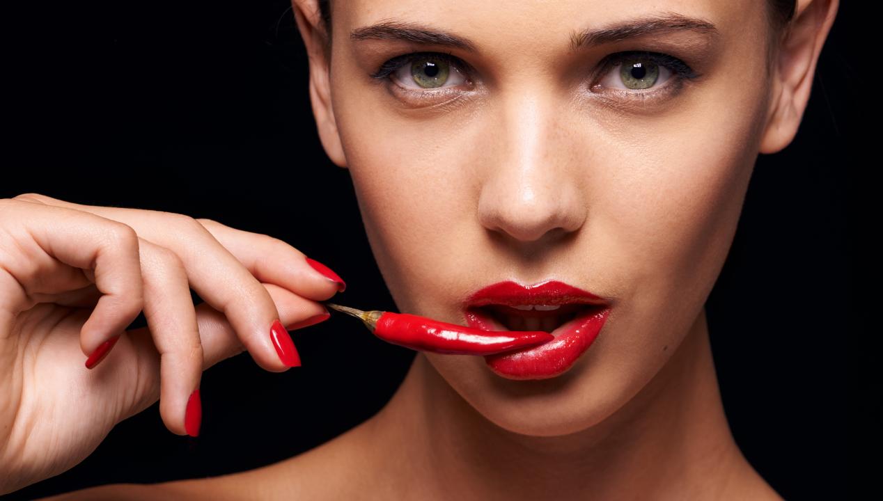 schöne Frau mit roten Lippen und Fingernägeln knabbert an einer roten Chili