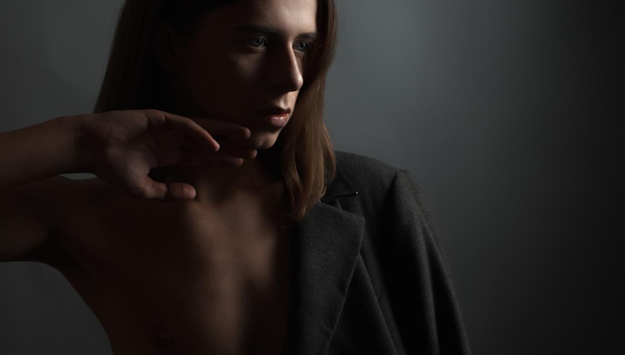 Femboy mit Blazer, nacktem Oberkörper und Hand am Mund