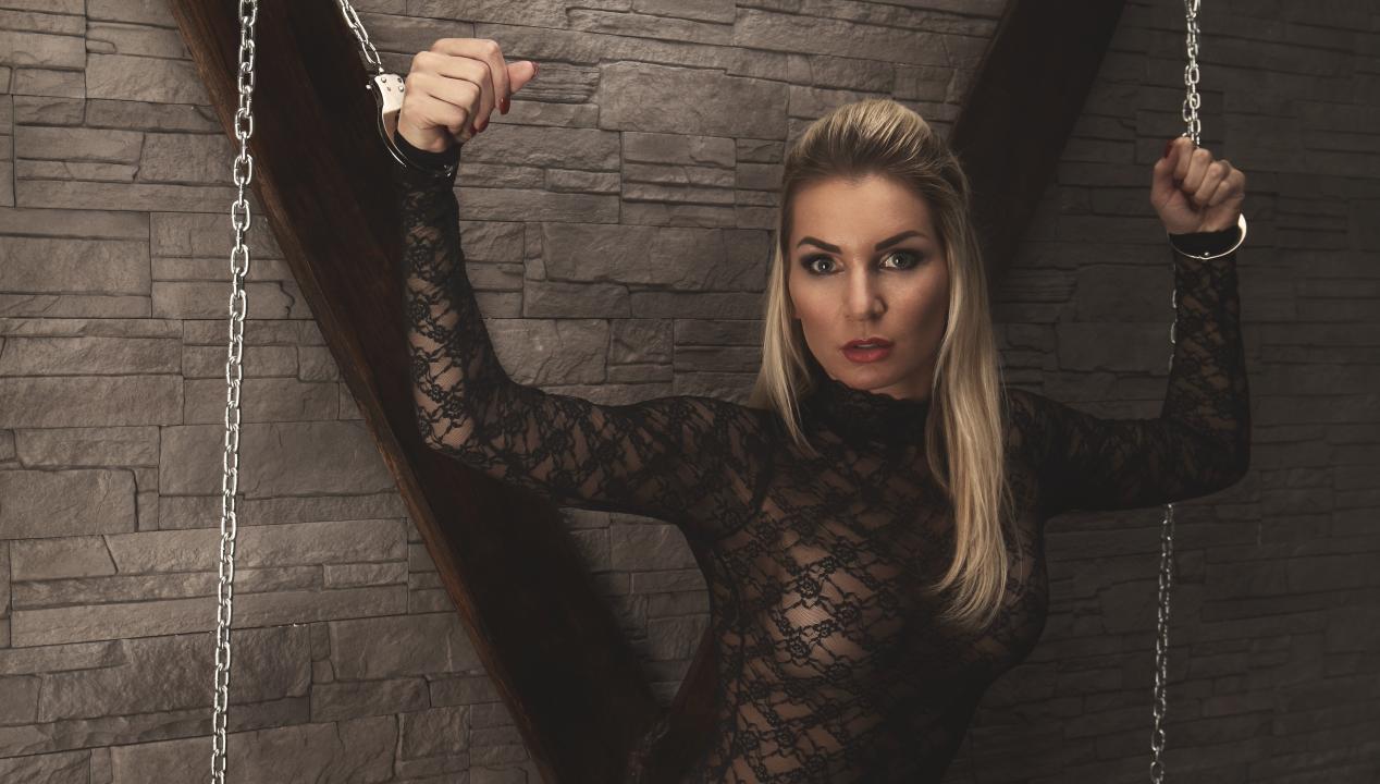 submissive Frau in Seidenbody wurde mit Ketten von einer Femdom an ein Andreaskreuz gefesselt - ein beliebtes Femdom-Sexgeschichten-Motiv