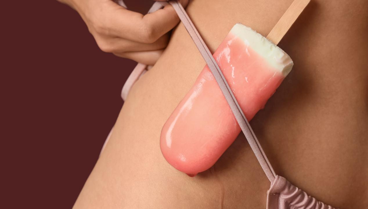 eine Frau steckt sich ein rosa Wassereis für eine Camsex-Session in das Seitenband ihres Bikini-Höschens