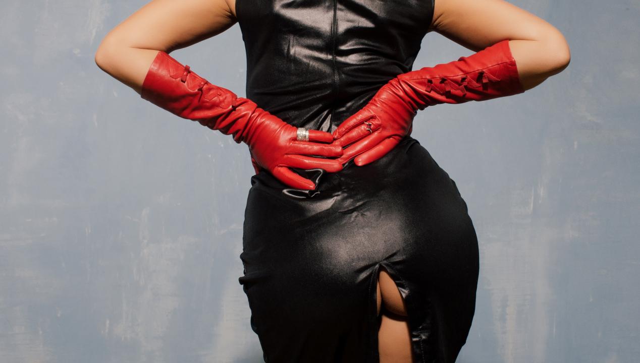 sexy asiatische Frau präsentiert ihren Rücken und Hitnern in einem schwarzen BDSM-Outfit mit roten Handschuhen